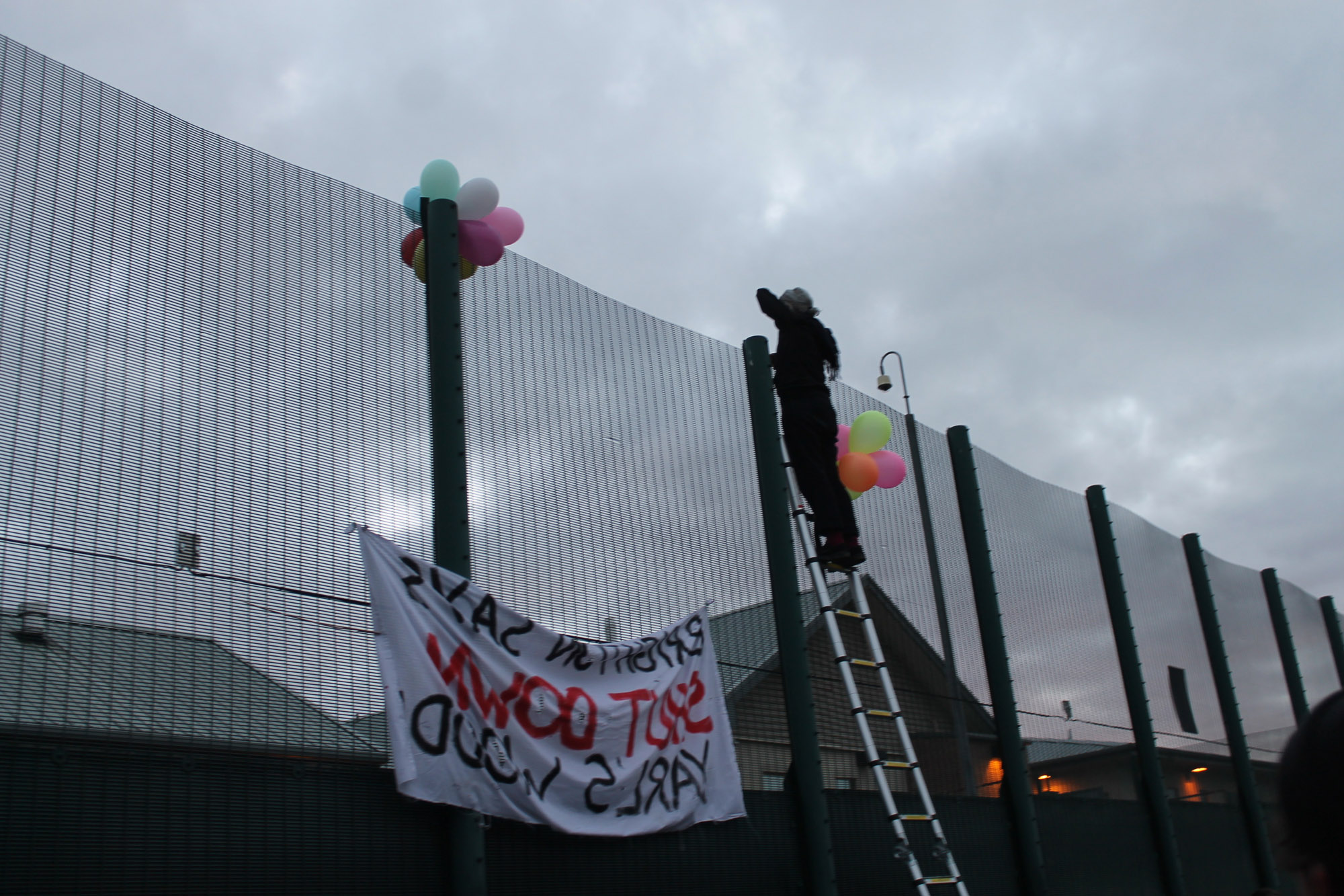 A man standing on a ladder at the barriers of yarls wood to show support to the detainees
