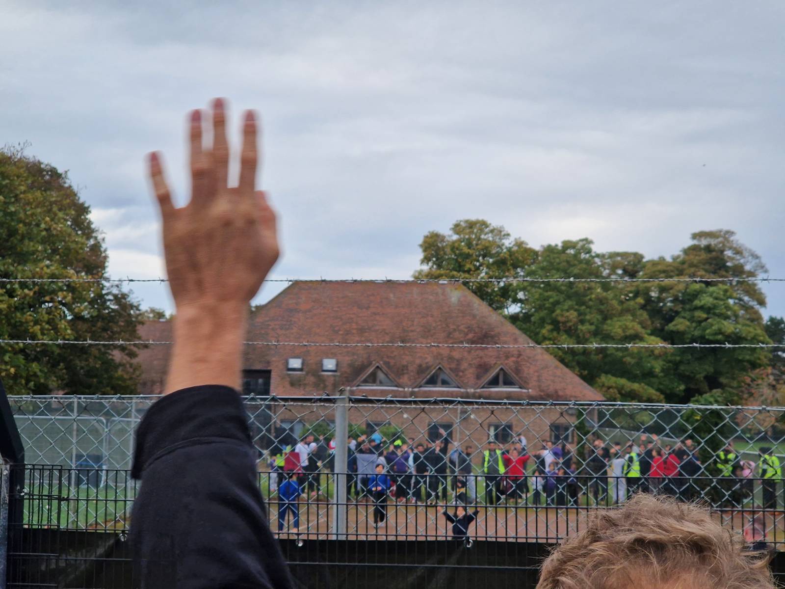 A protester waving to the people and children behind the barbed wire fence at Manston